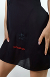 Detailed view of 'Take Me Off' embroidery paired with red floral stitching on sheer black dress